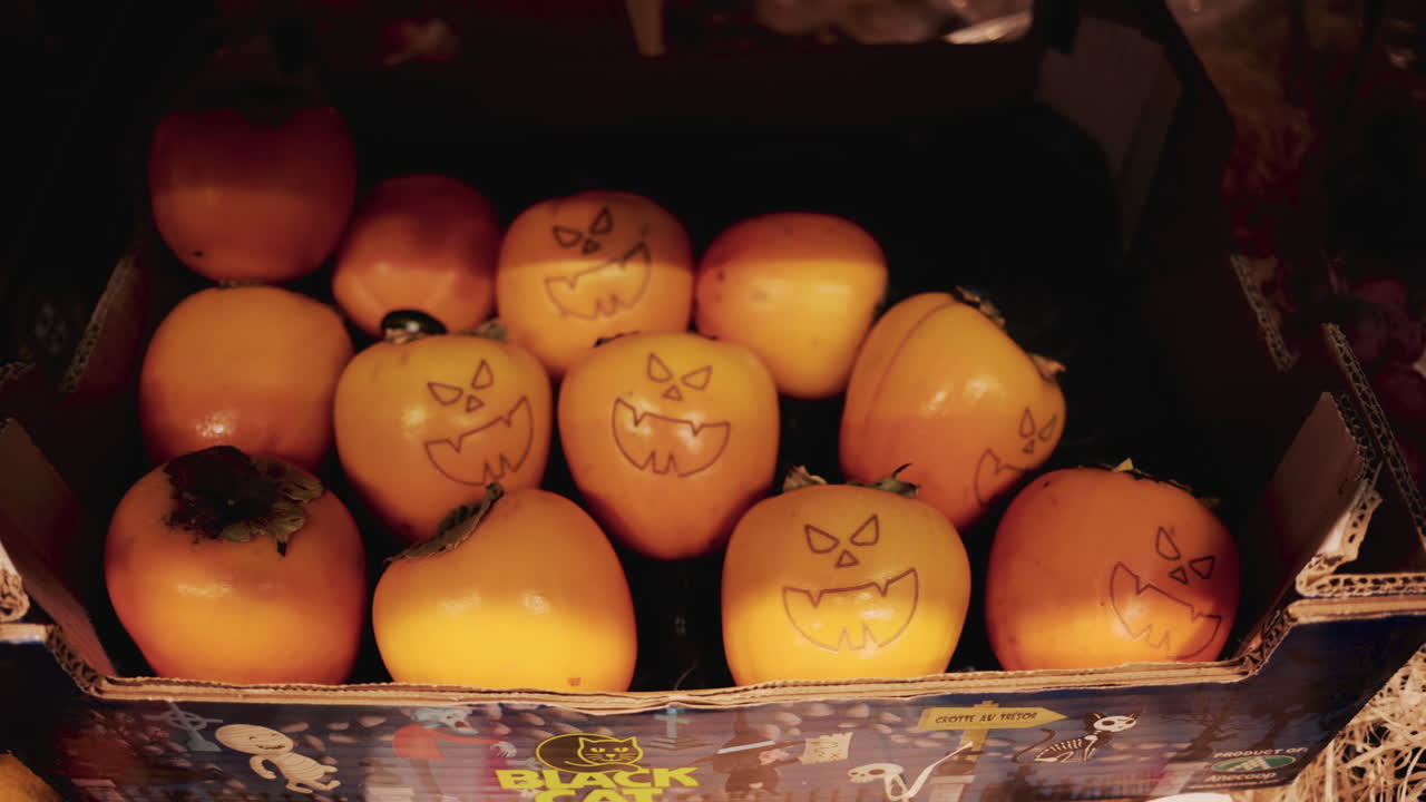 Hand holding a persimmon with a Halloween style jack o' lantern face drawn on it in a grocery store