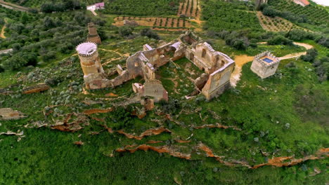 aerial drone backward moving shot of ruins of an old building on the hill top with a winding river flowing in the background in north of troina, sicily, italy withgreen vegetation on a cloudy day