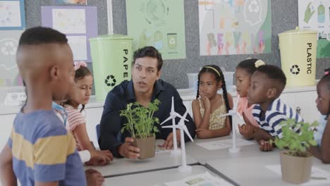 happy diverse male teacher teaching schoolchildren ecology with models in class at elementary school