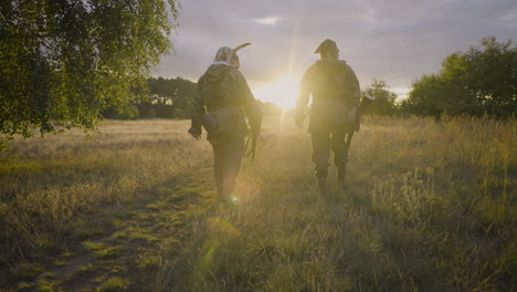 two hunters walking in a field at sunset