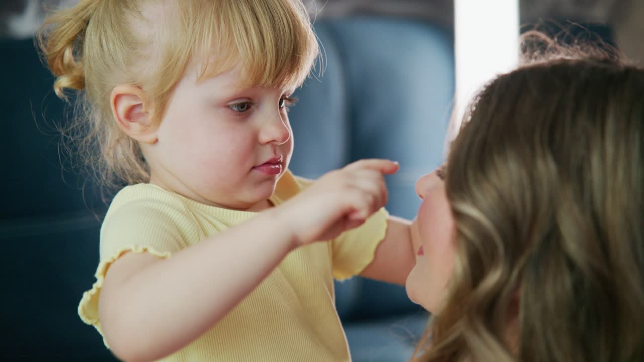 Una bambina in maglietta gialla guarda un'altra bambina. I suoi capelli sono raccolti in uno chignon. La seconda bambina le tocca delicatamente la mano. Entrambe le bambine sembrano curiose e coinvolte. La scena trasmette un'atmosfera calda e tenera.