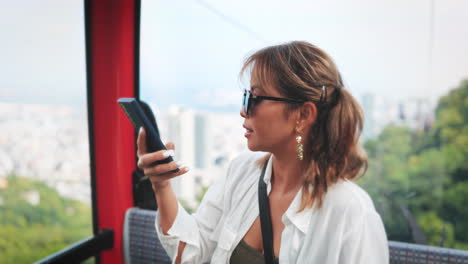 woman with light brown hair and sunglasses takes a selfie in a red cable car