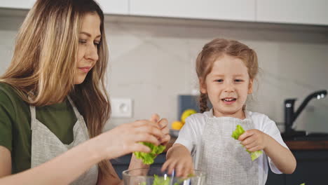 mujer con hija graciosa lágrima de lechuga hojas de cocina ensalada