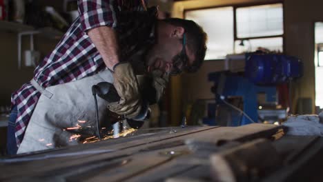 caucasian male knife maker in workshop wearing glasses and using angle grinder