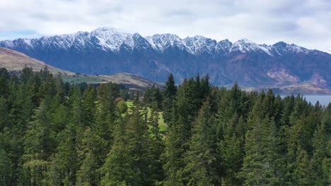 aerial shot over trees reveals queenstown new zealand and remarkables mountain range
