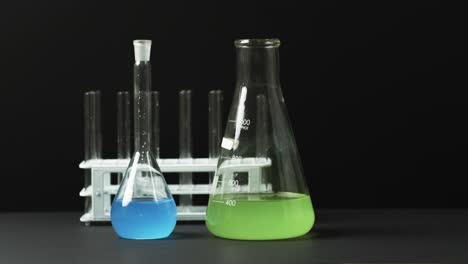 Coloured-liquids-in-flasks-with-test-tubes-in-stand-on-black-background-with-copy-space,-slow-motion