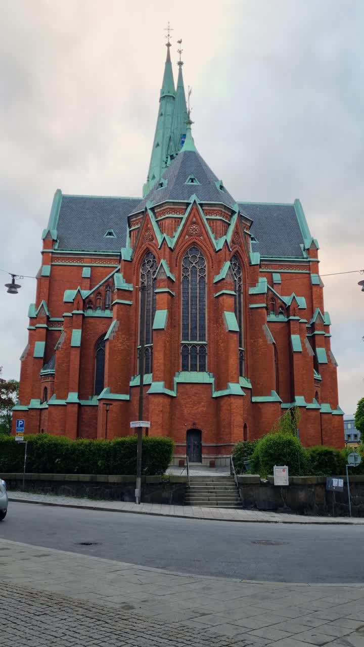 Vertical shot of the striking St. John’s Church in central Stockholm, Sweden, rising against a moody, cloud-filled evening sky, highlighting its Gothic Revival architecture and commanding presence