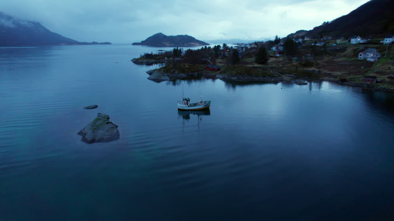Vista orbitale di un peschereccio che rivela un villaggio norvegese all'interno di un fiordo nella Norvegia settentrionale con un cielo drammatico