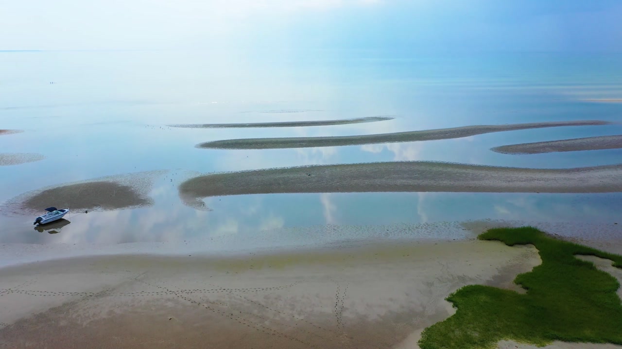 Aerial drone footage of a beach during low tide, with shallow tidal pools, rippled sands, and rolling dunes stretching into the horizon, creating a textured and cinematic seaside panorama view.
