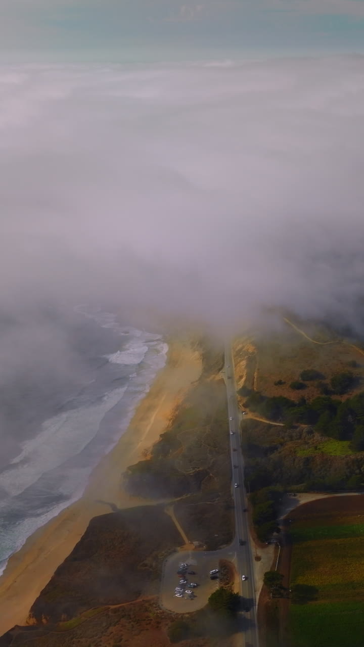 Beautiful coast with sandy beach, rocks and meadows in Montara, California, USA. Thick white fog spreading on the land from water. Aerial view. Vertical video