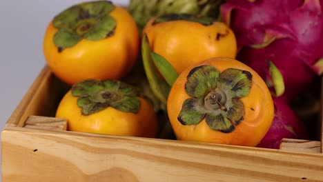 persimmons and dragon fruits in a wooden crate