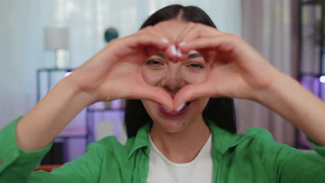 young woman makes symbol of love, showing heart sign to camera, express romantic positive feelings