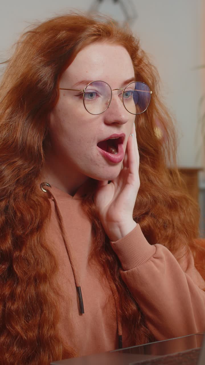 Surprised caucasian redhead woman with windswept hair using laptop sitting on couch at home