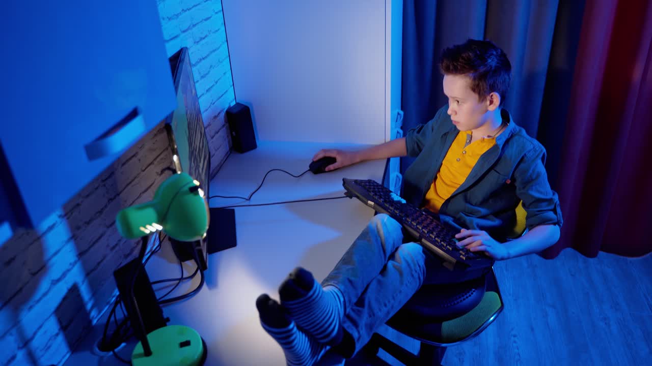 Un adolescente si sta divertendo con i videogiochi a casa. Un ragazzo gioca ai videogiochi per computer seduto sulla sedia con le gambe sulla scrivania. Vista dall'alto.