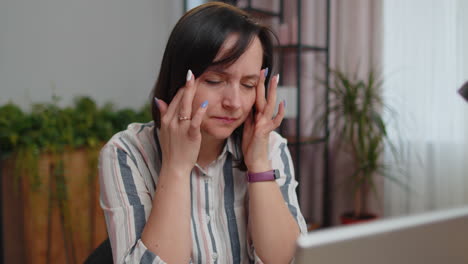 tired woman teacher using laptop computer suffering from tension, migaine headache at home office