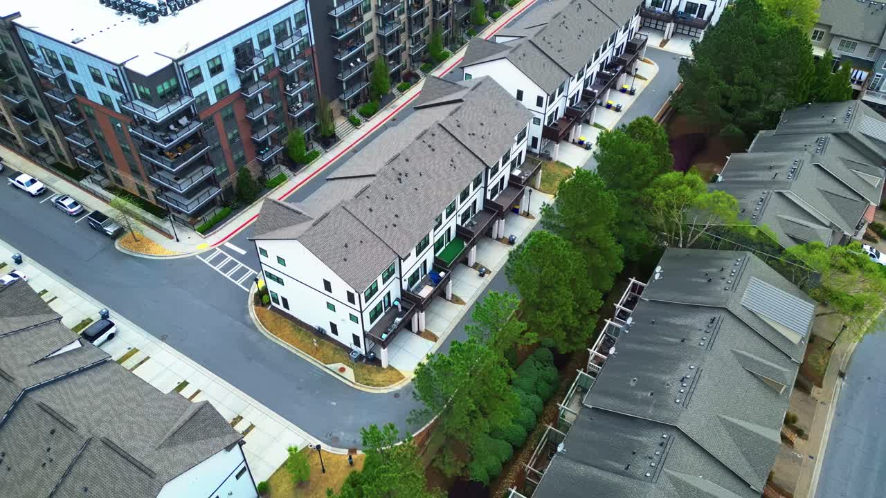 Townhouse Condos and row of two-story houses during sunny day in american neighborhood. Aerial tilt up wide shot. Sunny day with green trees and parking cars.