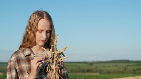 portrait of a cute girl with a bouquet of spikelets on the background of a wheat field