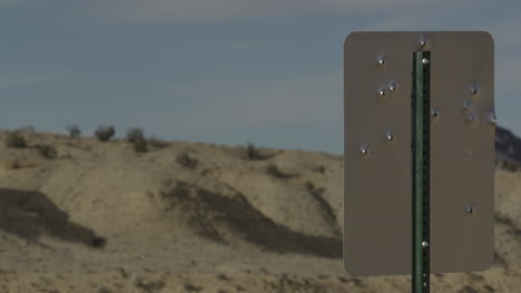 sign in the desert with bullet holes