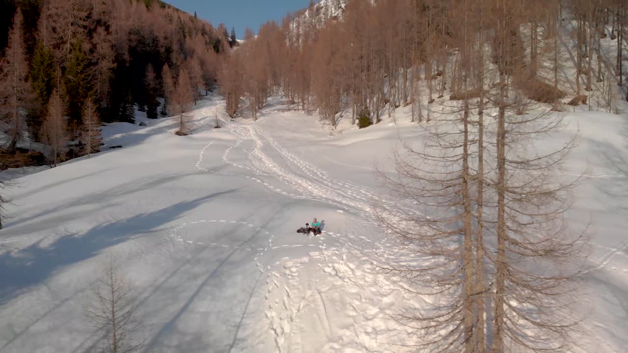 volando lejos de un hombre sentado en la nieve en las montañas mientras la cámara se aleja mostrando las montañas y las rutas de senderismo