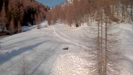 Volando-Lejos-De-Un-Hombre-Sentado-En-La-Nieve-En-Las-Montañas-Mientras-La-Cámara-Se-Aleja-Mostrando-Las-Montañas-Y-Las-Rutas-De-Senderismo