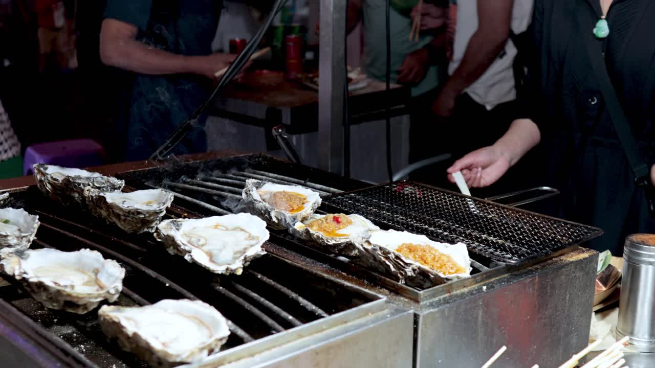 Oysters being grilled and seasoned at a market