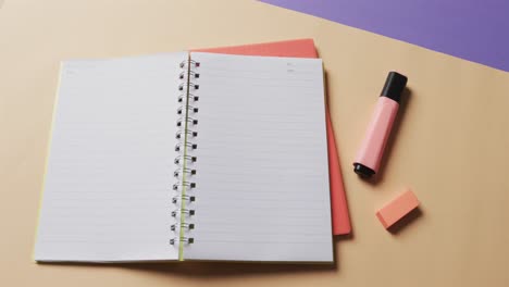 Overhead-view-of-open-notebook-with-school-stationery-on-beige-and-blue-background,-in-slow-motion