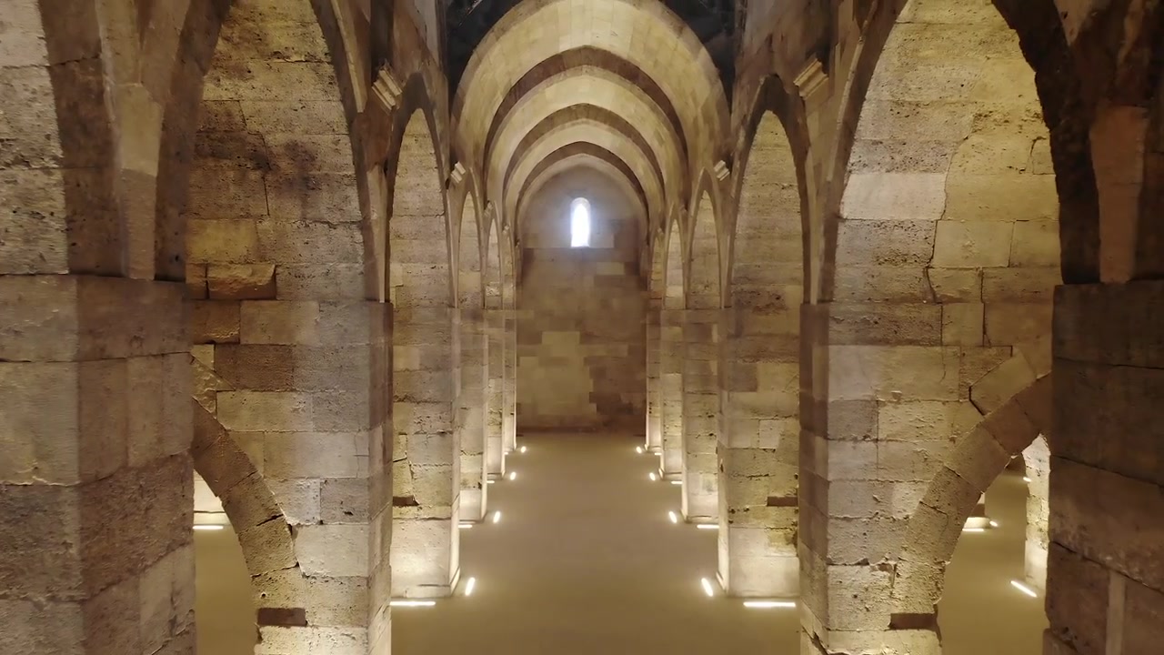 Vista interna di un'antica sala a volta in pietra con archi.