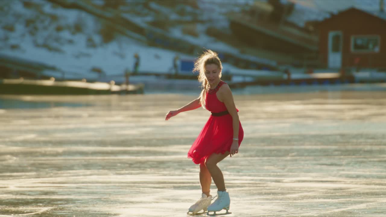 Kaunis taitoluistelija liukuu tyylikkäästi kimaltelevalla jääpinnalla esitellen dynaamista asentoa kirkkaanpunaisessa mekossa vangiten taiteellisuuden ja liikkeen olemuksen kauniina talvipäivänä.