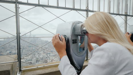 mujer rubia mirando a través de binoculares en el panorama de nueva york visite el concepto de nueva york