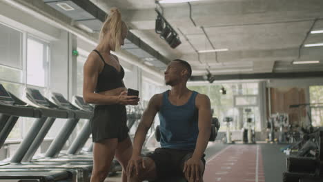 caucasian female monitor and an athletic african american man talking in the gym.