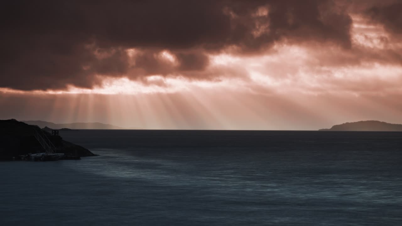 The orange and pink tones of sunset reflect on the water as the sun disappears behind Norwegian islands