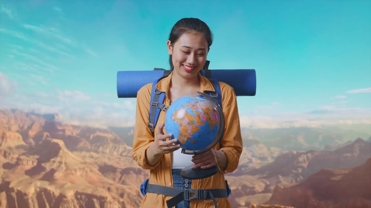 Asian Female Hiker With Mountaineering Backpack Holding World Globe In Her Hands And Smiling While Traveling At The Top Of Mountain