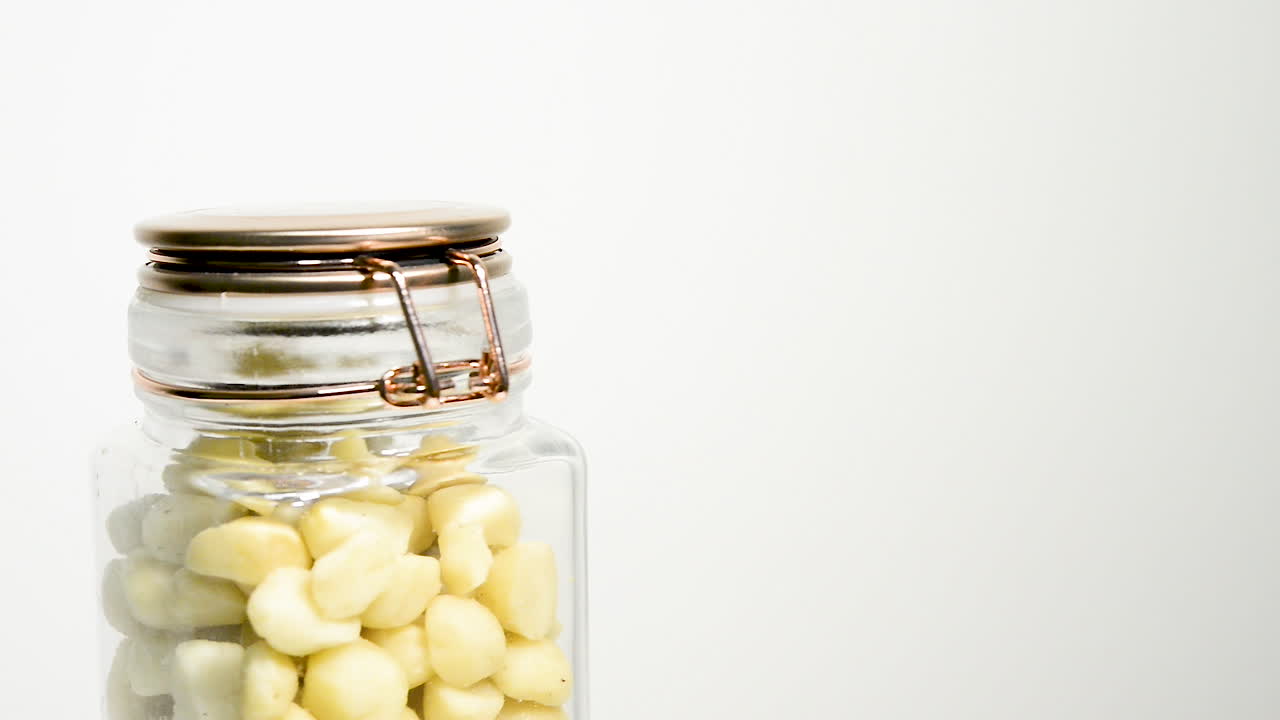 흰색 배경에 시계 반대 방향으로 천천히 회전하는 마카다미아 너트 한 병