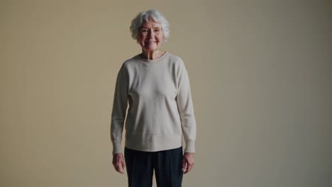 confident senior woman with short gray hair wearing beige sweater, standing against neutral background in authentic studio portrait representing graceful aging