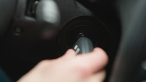 close up of urban explorer inserting metal key into ignition starter and turning key inside vehicle cabin focusing on hand movement dashboard blur and winter jacket sleeve before engine start signal