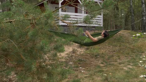 a man in a hammock hangs on trees while drinking at the backyard of a house at norwegian village in arendel, zagorow poland