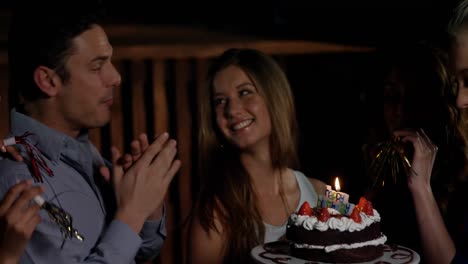 group of smiling friends blowing candle while celebrating birthday in bar