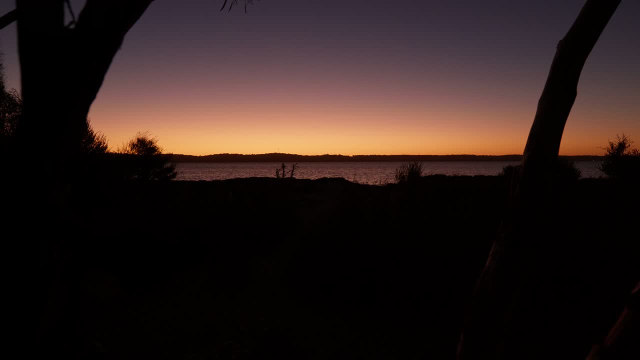A stunning orange glow from the sunset beyond a serene lake, casting beautiful reflections across the calm water.