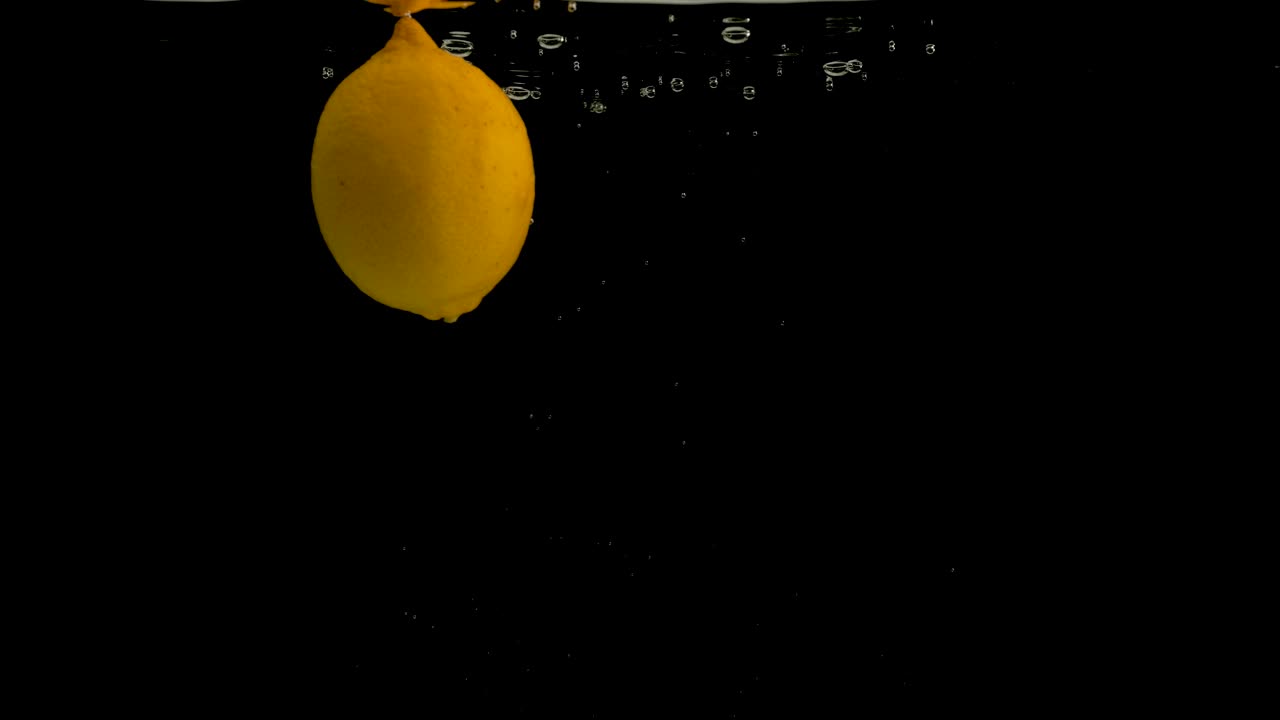 Lemons falling into water on black background. Bright high quality video