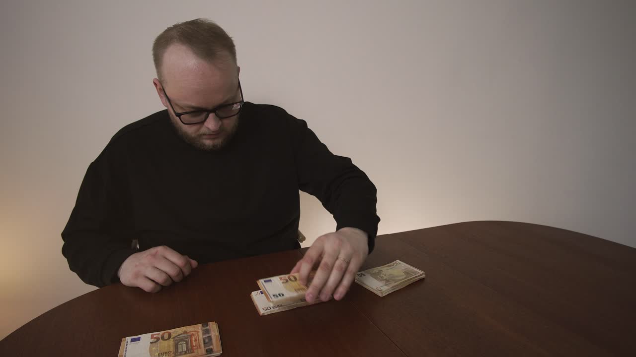 Uomo che imposta il bilancio familiare con banconote in euro sul tavolo. Concetto di budgeting, pianificazione delle spese e gestione delle finanze personali a casa.