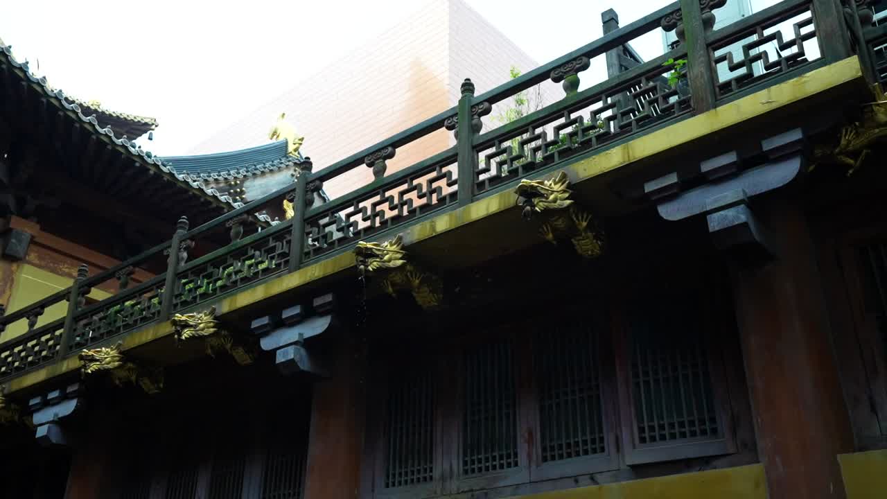 Golden dragon shaped pipes pour rainwater from a balcony of Jingan Temple on a rainy day, Shanghai, China