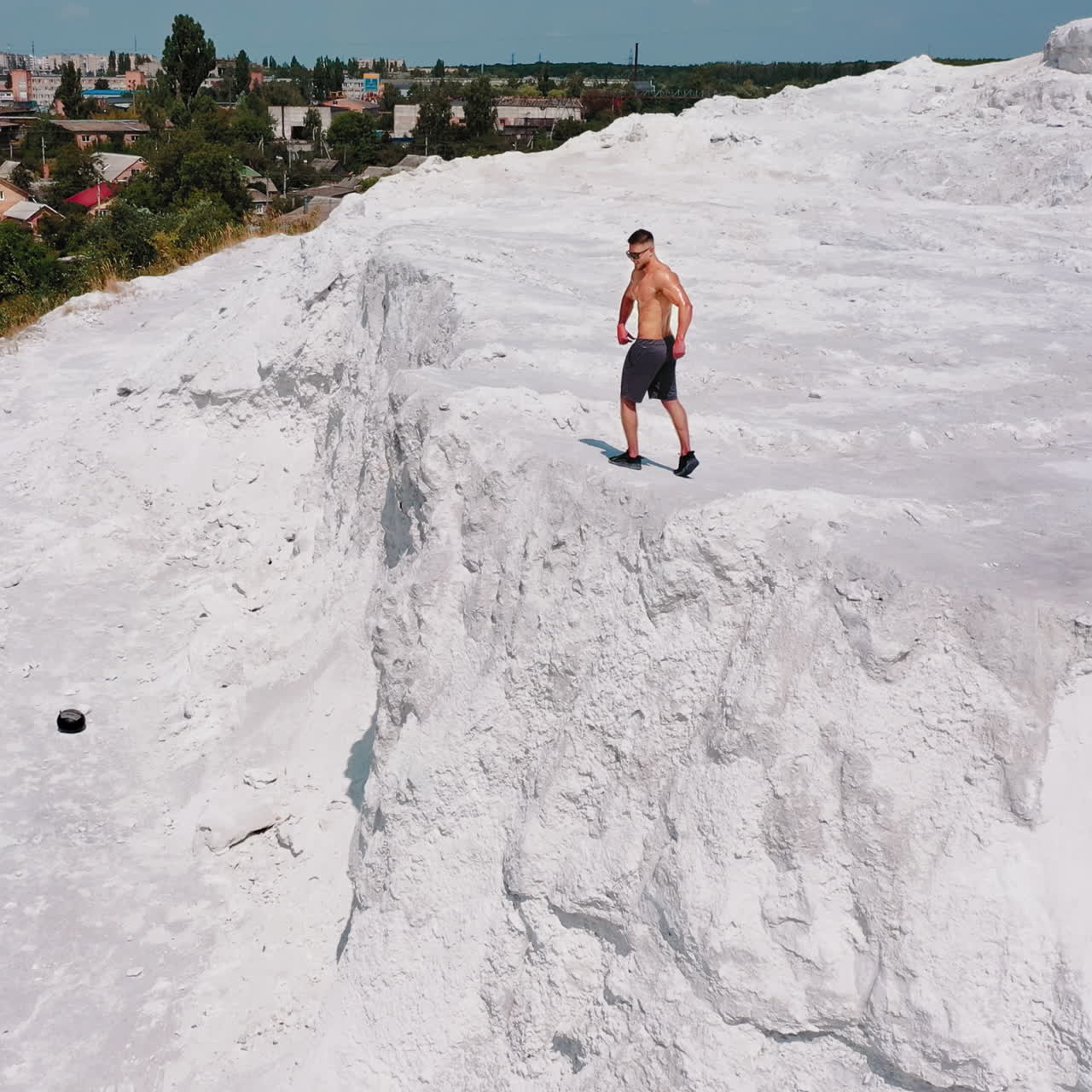 Brutal strong bodybuilder posing outdoor. Photoshoot in a quarry. Outdoor sports concept. Aerial view. Posing and pumping muscles. White landscape.