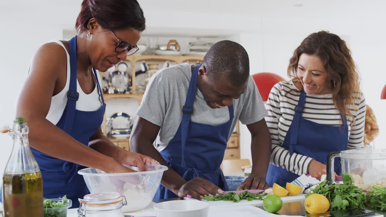 Male And Female Adult Students Preparing Ingredients For Dish In Kitchen Cookery Class