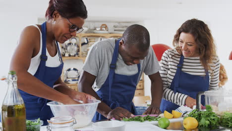 Male-And-Female-Adult-Students-Preparing-Ingredients-For-Dish-In-Kitchen-Cookery-Class