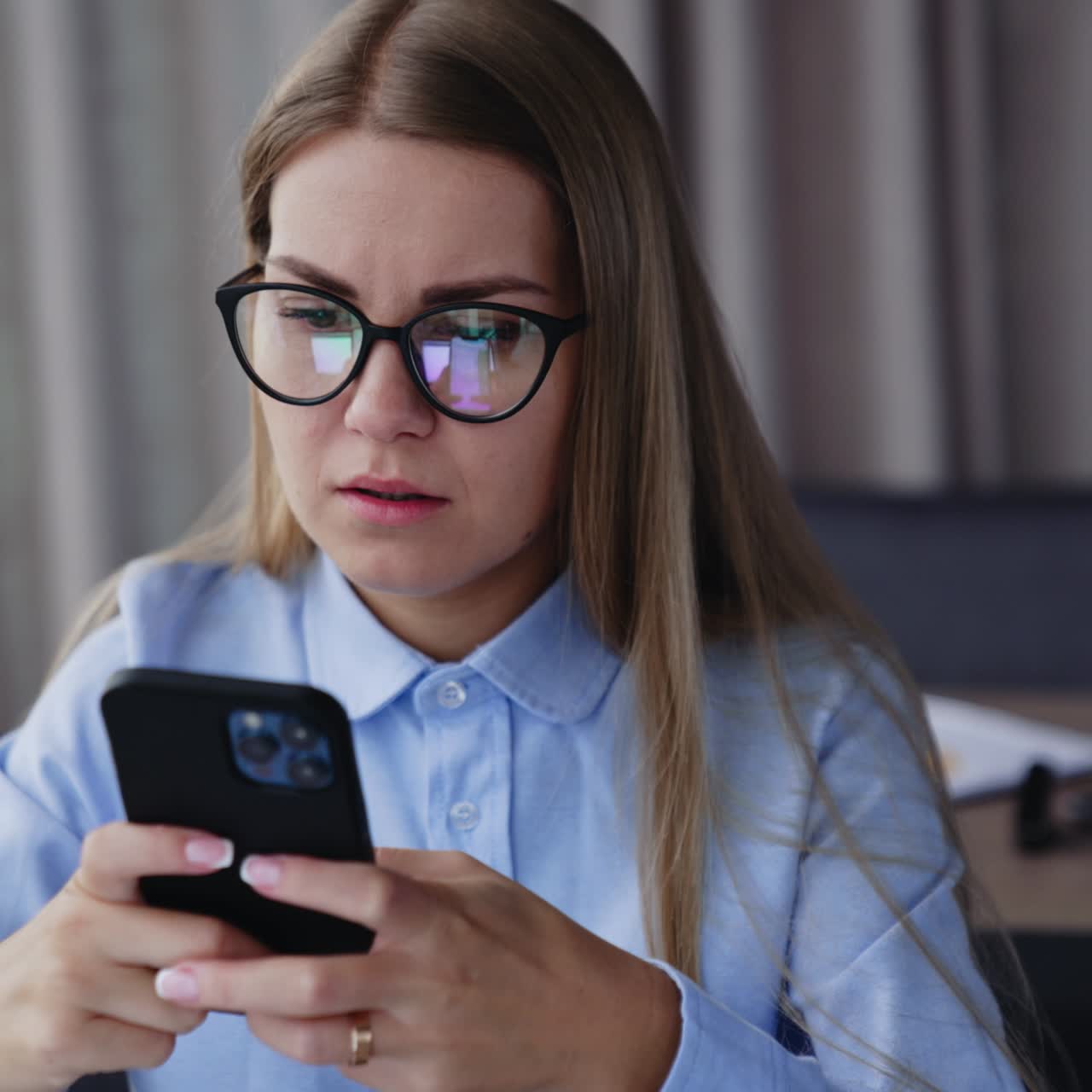 Concerned long-haired woman looking on the phone she's holding in both hands. Worried lady reading news on the smartphone