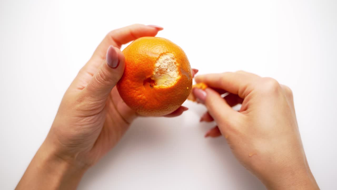Woman cleans tangerine on the table. Top view of female's hands holds sweet citrus. Hands are peeling fresh mandarin. Close-up.