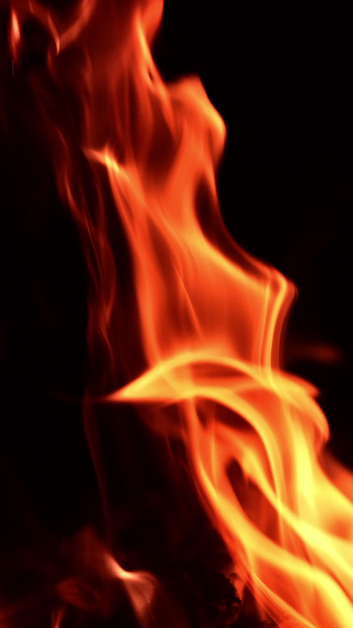 Fire flames rising diagonally in the air. Bonfire burning isolated at black backdrop. Vertical video