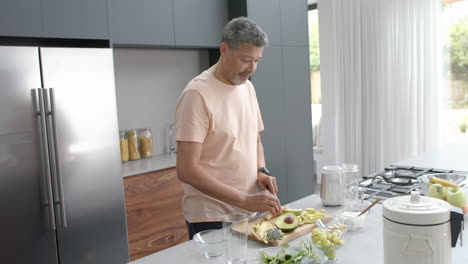 Happy-senior-biracial-man-preparing-ingredients-for-healthy-smoothie-in-kitchen-at-home,-slow-motion