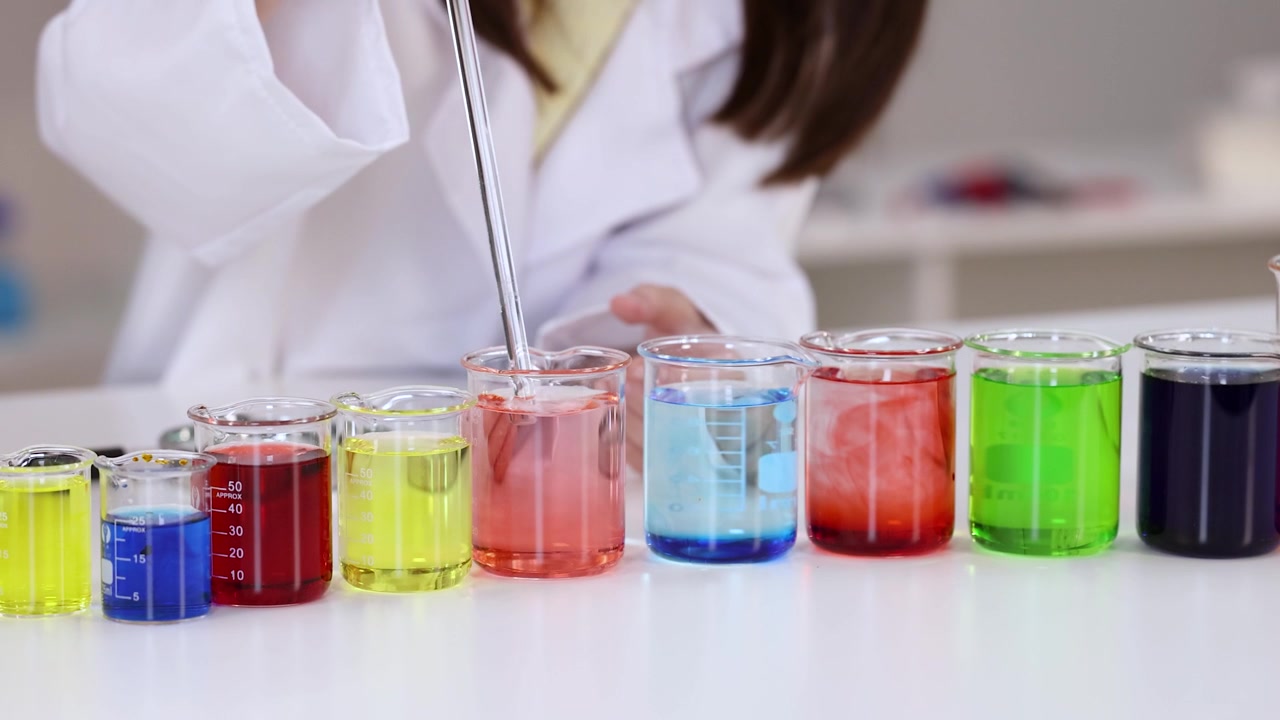 Primo piano di uno scienziato in camice bianco da laboratorio che mescola liquidi vivaci in becher di vetro