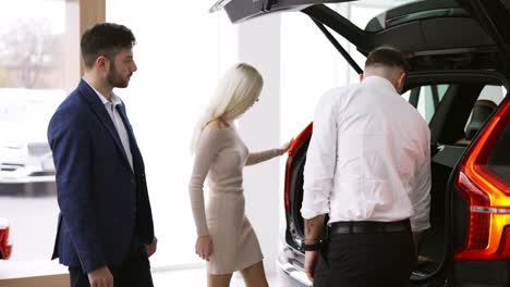 salesman showing the capacity of a trunk from inside to customers in car showroom, side view